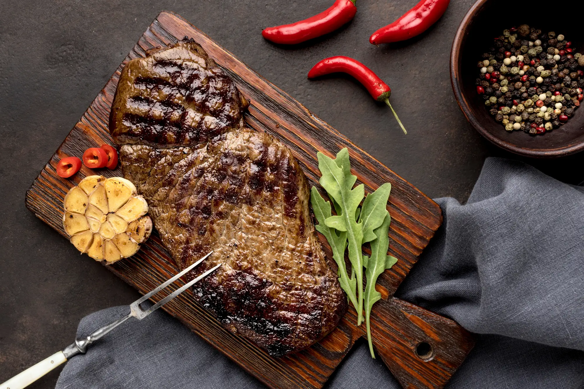 Grilled steak on a wooden board with garlic, chilli and rocket